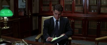 Movie still from “The Rainmaker” (1997), directed by Francis Ford Coppola – A man in a suit and tie writing on a piece of paper; Medium shot, Over the shoulder angle