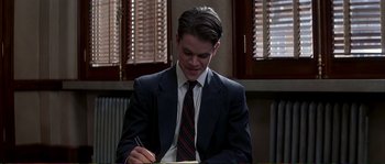 Movie still from “The Rainmaker” (1997), directed by Francis Ford Coppola – A man in a suit and tie writing on a piece of paper; Medium shot, Low angle