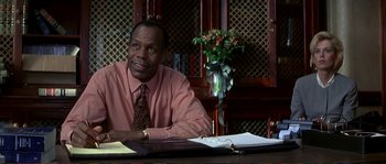 Movie still from “The Rainmaker” (1997), directed by Francis Ford Coppola – A man sitting at a desk in front of papers; Medium shot, Over the shoulder angle