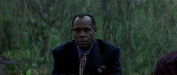 Movie still from “The Rainmaker” (1997), directed by Francis Ford Coppola – A man in a suit and tie sitting in a wooded area; Close Up shot, Low angle