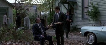 Movie still from “The Rainmaker” (1997), directed by Francis Ford Coppola – A man in a suit and tie holding a plate of food; Wide shot, Over the shoulder angle