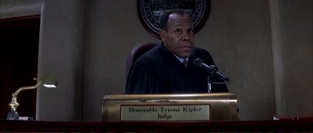 Movie still from “The Rainmaker” (1997), directed by Francis Ford Coppola – A judge is sitting at a podium in front of a microphone; Medium shot, High angle