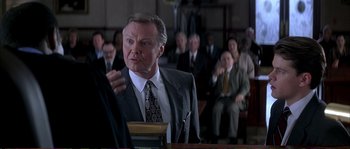 Movie still from “The Rainmaker” (1997), directed by Francis Ford Coppola – A man in a suit and tie in front of a group of people; Medium shot, Over the shoulder angle
