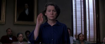 Movie still from “The Rainmaker” (1997), directed by Francis Ford Coppola – A woman is holding her hand up in the air while wearing a blue shirt; Medium shot, Low angle