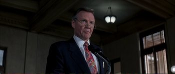 Movie still from “The Rainmaker” (1997), directed by Francis Ford Coppola – A man in a suit and tie is speaking at a podium; Close Up shot, Low angle