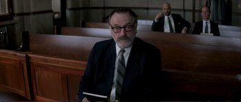 Movie still from “The Rainmaker” (1997), directed by Francis Ford Coppola – A man in a suit and tie sitting in a courtroom; Medium shot, Over the shoulder angle