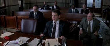 Movie still from “The Rainmaker” (1997), directed by Francis Ford Coppola – A man sitting at a table in front of a microphone; Medium shot, Low angle