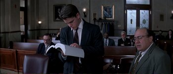 Movie still from “The Rainmaker” (1997), directed by Francis Ford Coppola – A man in a suit reading a book in front of a crowd; Medium shot, Low angle