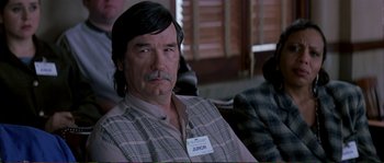 Movie still from “The Rainmaker” (1997), directed by Francis Ford Coppola – A man with long black hair wearing a name tag; Medium shot, High angle