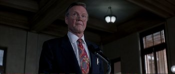 Movie still from “The Rainmaker” (1997), directed by Francis Ford Coppola – A man in a suit and tie standing in front of a microphone; Close Up shot, Low angle