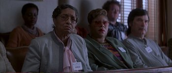 Movie still from “The Rainmaker” (1997), directed by Francis Ford Coppola – A group of people sitting next to each other in a room; Close Up shot, High angle