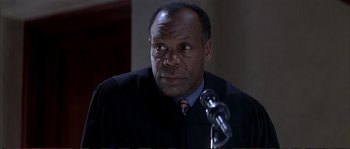 Movie still from “The Rainmaker” (1997), directed by Francis Ford Coppola – A man wearing a black robe is sitting in front of a microphone; Close Up shot, Low angle