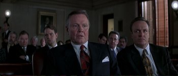Movie still from “The Rainmaker” (1997), directed by Francis Ford Coppola – A man in a suit and tie in front of a group of people; Close Up shot, Low angle