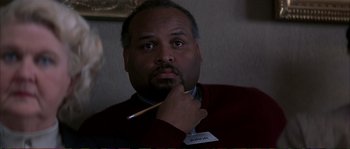 Movie still from “The Rainmaker” (1997), directed by Francis Ford Coppola – A man holding a pencil in his hand while wearing a red sweater; Close Up shot, Over the shoulder angle