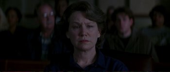 Movie still from “The Rainmaker” (1997), directed by Francis Ford Coppola – An older woman is sitting in front of a group of people; Close Up shot, Over the shoulder angle