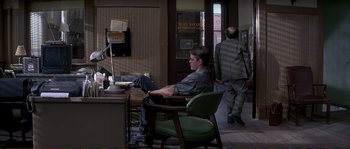 Movie still from “The Rainmaker” (1997), directed by Francis Ford Coppola – A man sitting in a chair in a room; Wide shot, High angle