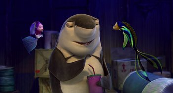 Movie still from “Shark Tale” (2004), directed by Vicky Jenson – A shark is holding a drink in front of some fish; Medium shot, Over the shoulder angle