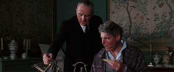 Movie still from “The Remains of the Day” (1993), directed by James Ivory – Two men in suits are looking at each other while eating; Medium shot, Over the shoulder angle