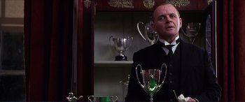 Movie still from “The Remains of the Day” (1993), directed by James Ivory – A man standing in front of a table holding a trophy; Medium shot, Low angle