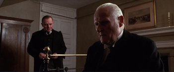 Movie still from “The Remains of the Day” (1993), directed by James Ivory – An older man in a suit and tie playing the piano; Medium shot, Over the shoulder angle