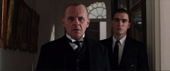 Movie still from “The Remains of the Day” (1993), directed by James Ivory – A man in a suit and tie standing next to another man in a suit and tie; Close Up shot, Low angle