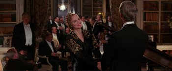 Movie still from “The Remains of the Day” (1993), directed by James Ivory – A woman in a black and gold dress smiling; Medium shot, Over the shoulder angle