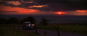 Movie still from “The Remains of the Day” (1993), directed by James Ivory – An old car parked on the side of the road at sunset; Extreme Wide shot, High angle