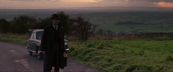 Movie still from “The Remains of the Day” (1993), directed by James Ivory – A man in a suit and hat is standing on the side of the road; Wide shot, Over the shoulder angle