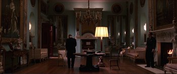 Movie still from “The Remains of the Day” (1993), directed by James Ivory – A man standing in front of a fireplace in a room; Wide shot, Low angle