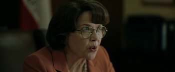 Movie still from “The Report” (2019), directed by Scott Z. Burns – An older woman wearing glasses and a brown jacket; Close Up shot, Over the shoulder angle