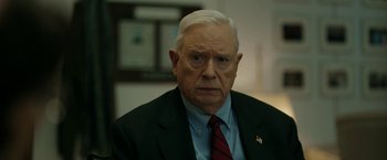 Movie still from “The Report” (2019), directed by Scott Z. Burns – An older man wearing a suit and tie; Close Up shot, Over the shoulder angle