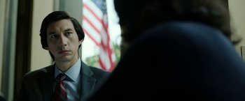 Movie still from “The Report” (2019), directed by Scott Z. Burns – A man wearing a suit and tie in front of an american flag; Close Up shot, Low angle