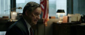 Movie still from “The Report” (2019), directed by Scott Z. Burns – An older man wearing a suit and red tie; Close Up shot, Over the shoulder angle