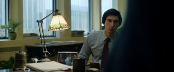 Movie still from “The Report” (2019), directed by Scott Z. Burns – A man sitting at a table in front of a lamp; Medium shot, Over the shoulder angle