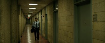 Movie still from “The Report” (2019), directed by Scott Z. Burns – A man walking down a hallway holding a bag of luggage; Wide shot, Low angle
