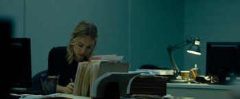 Movie still from “The Report” (2019), directed by Scott Z. Burns – A woman sitting at a desk with papers and papers; Medium shot, Over the shoulder angle