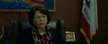 Movie still from “The Report” (2019), directed by Scott Z. Burns – An older woman sitting in an office chair wearing glasses; Close Up shot, Over the shoulder angle