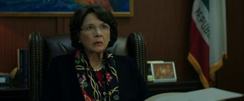 Movie still from “The Report” (2019), directed by Scott Z. Burns – An older woman sitting in a chair in a room; Close Up shot, Over the shoulder angle
