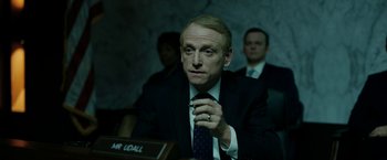 Movie still from “The Report” (2019), directed by Scott Z. Burns – A man in a suit and tie sitting in front of a board; Medium shot, Over the shoulder angle