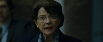 Movie still from “The Report” (2019), directed by Scott Z. Burns – An older woman wearing glasses and a jacket; Close Up shot, Over the shoulder angle