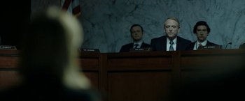 Movie still from “The Report” (2019), directed by Scott Z. Burns – Two men in suits sitting in front of a microphone; Medium shot, Over the shoulder angle