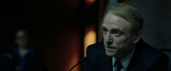 Movie still from “The Report” (2019), directed by Scott Z. Burns – A man in a suit and tie is sitting in front of a microphone; Close Up shot, Over the shoulder angle