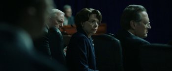Movie still from “The Report” (2019), directed by Scott Z. Burns – An older woman wearing glasses is sitting at a table; Close Up shot, Over the shoulder angle
