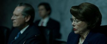 Movie still from “The Report” (2019), directed by Scott Z. Burns – A woman with glasses is sitting in front of two other men; Close Up shot, Over the shoulder angle