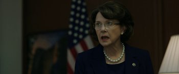 Movie still from “The Report” (2019), directed by Scott Z. Burns – An older woman wearing glasses and a pearl necklace; Close Up shot, Over the shoulder angle