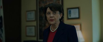 Movie still from “The Report” (2019), directed by Scott Z. Burns – An older woman wearing a red shirt and a black jacket; Close Up shot, Low angle