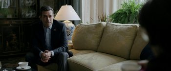 Movie still from “The Report” (2019), directed by Scott Z. Burns – A man in a suit sitting on a couch in front of a lamp; Medium shot, Over the shoulder angle
