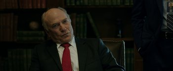 Movie still from “The Report” (2019), directed by Scott Z. Burns – An older man wearing a suit and red tie; Close Up shot, Over the shoulder angle