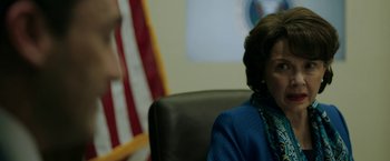 Movie still from “The Report” (2019), directed by Scott Z. Burns – A person sitting in front of an american flag; Close Up shot, Over the shoulder angle