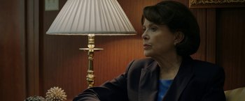Movie still from “The Report” (2019), directed by Scott Z. Burns – A woman sitting in front of a lamp in a room; Close Up shot, Over the shoulder angle